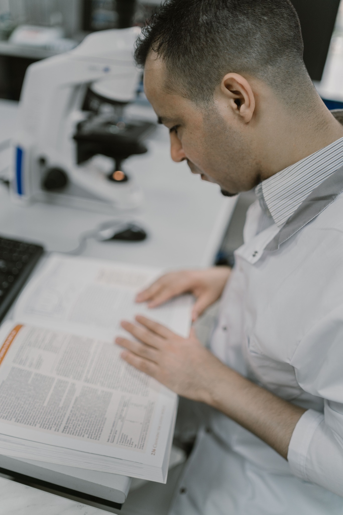A researcher reading an academic journal beside a microscope